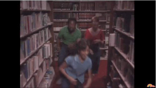 A man, woman, and child dancing through the isle of a library.
