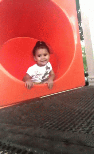 Little girl waving goodbye as she slides backwards down a playground slide.