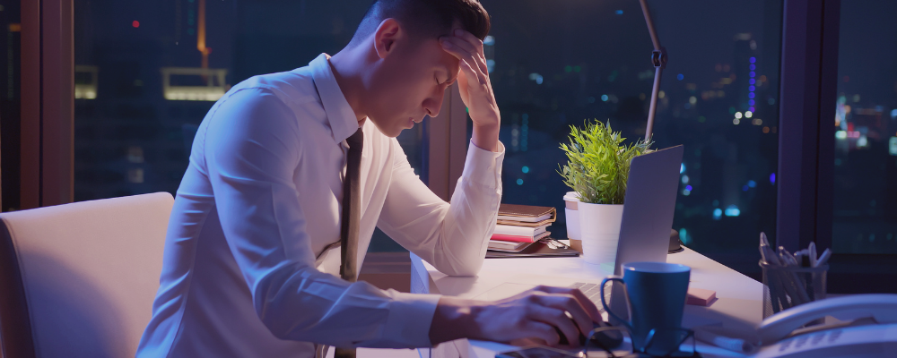Man sitting at his desk late at night holding his head in his hands