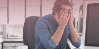 Man sitting at desk rubbing eyes stressed out due to poor mental health