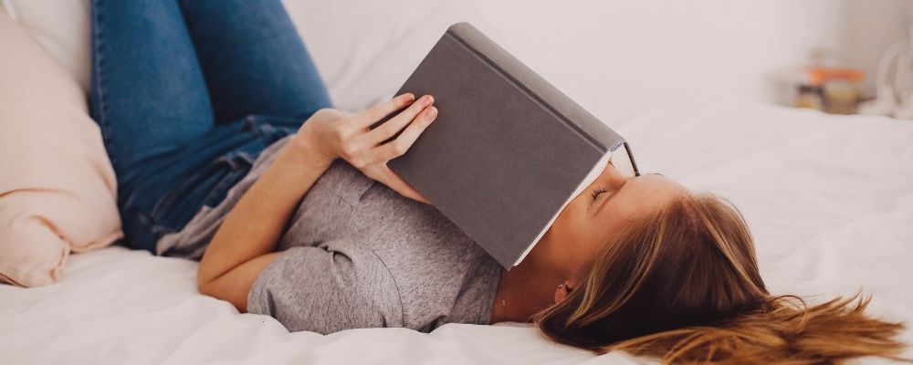 Woman laying on bed with a book relaxing as she tries moving past burnout