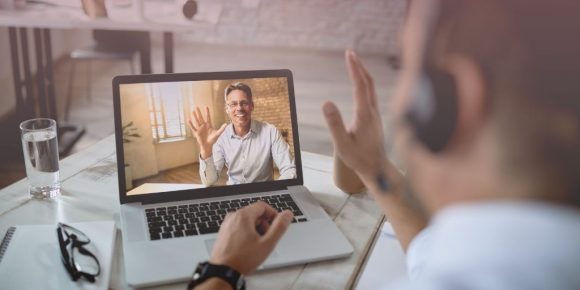 Remote employee waving to another worker through video conferencing to celebrate going remote