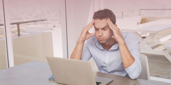 Frustrated man holds temples and makes a face as he waits for computer to load