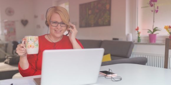 Woman at desk saying hello on a remote work meeting