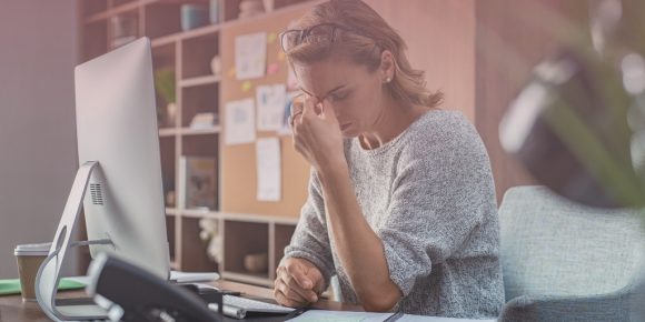 Female freelancer rubs her eyes as she sits at her desk looking mentally exhausted