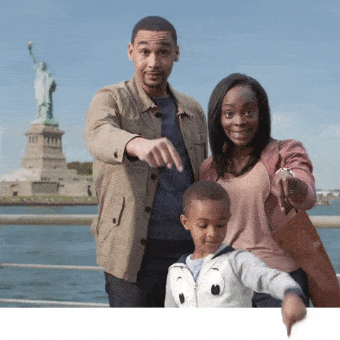 A family standing in front of the statue of liberty pointing down
