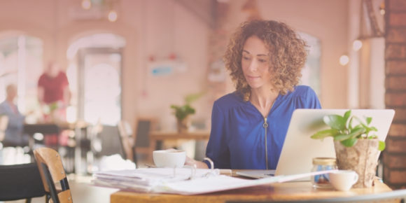 Woman looking through paperwork as she works on a laptop computer