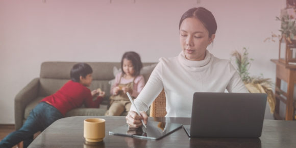 Woman in white shirt drawing on tablet for work while children play behind her